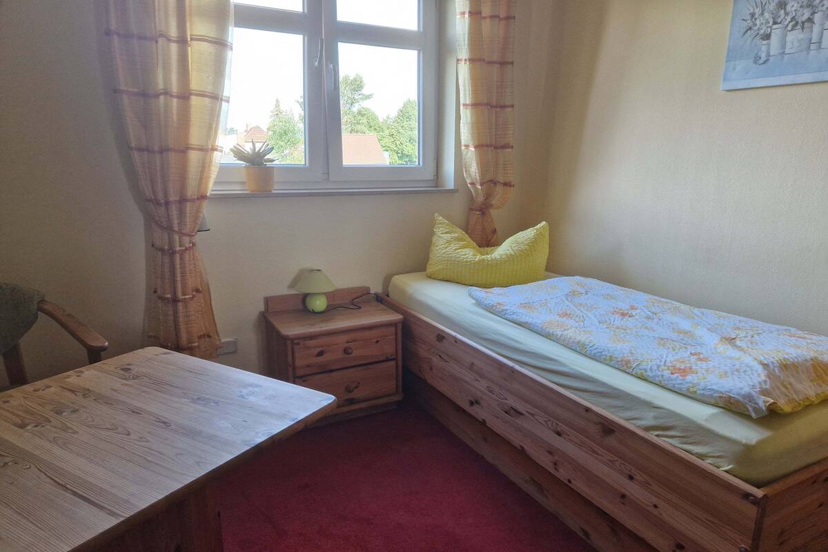 Une chambre à coucher avec un lit en bois, une table de chevet, un bureau et une fenêtre avec des rideaux.