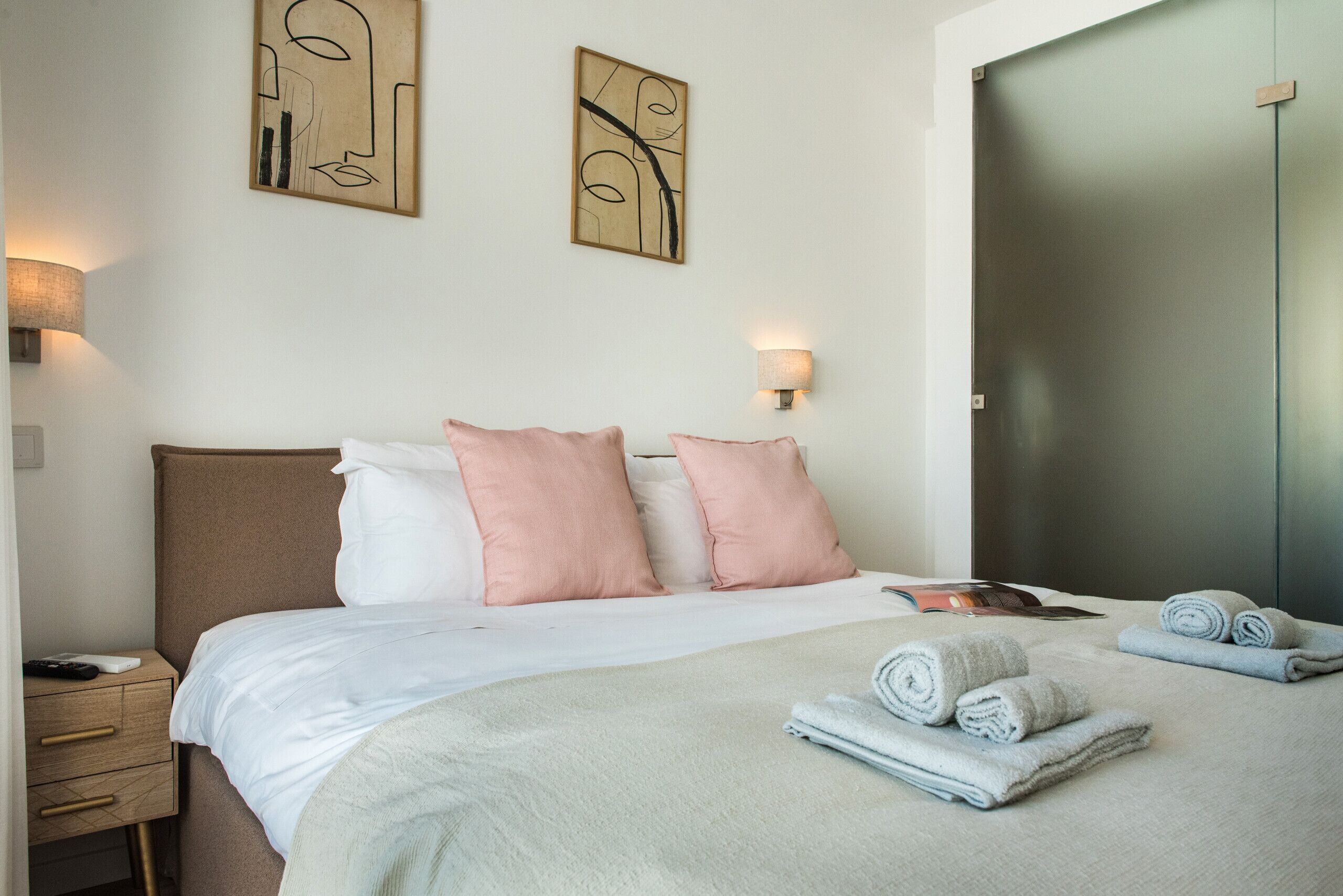A hotel room with a bed, pillows, a bedside table, a lamp, and a wardrobe.