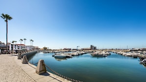 A marina with boats docked, a clear sky, and a paved walkway with bollards. - Faro Downtown - F in Faro (Faro)