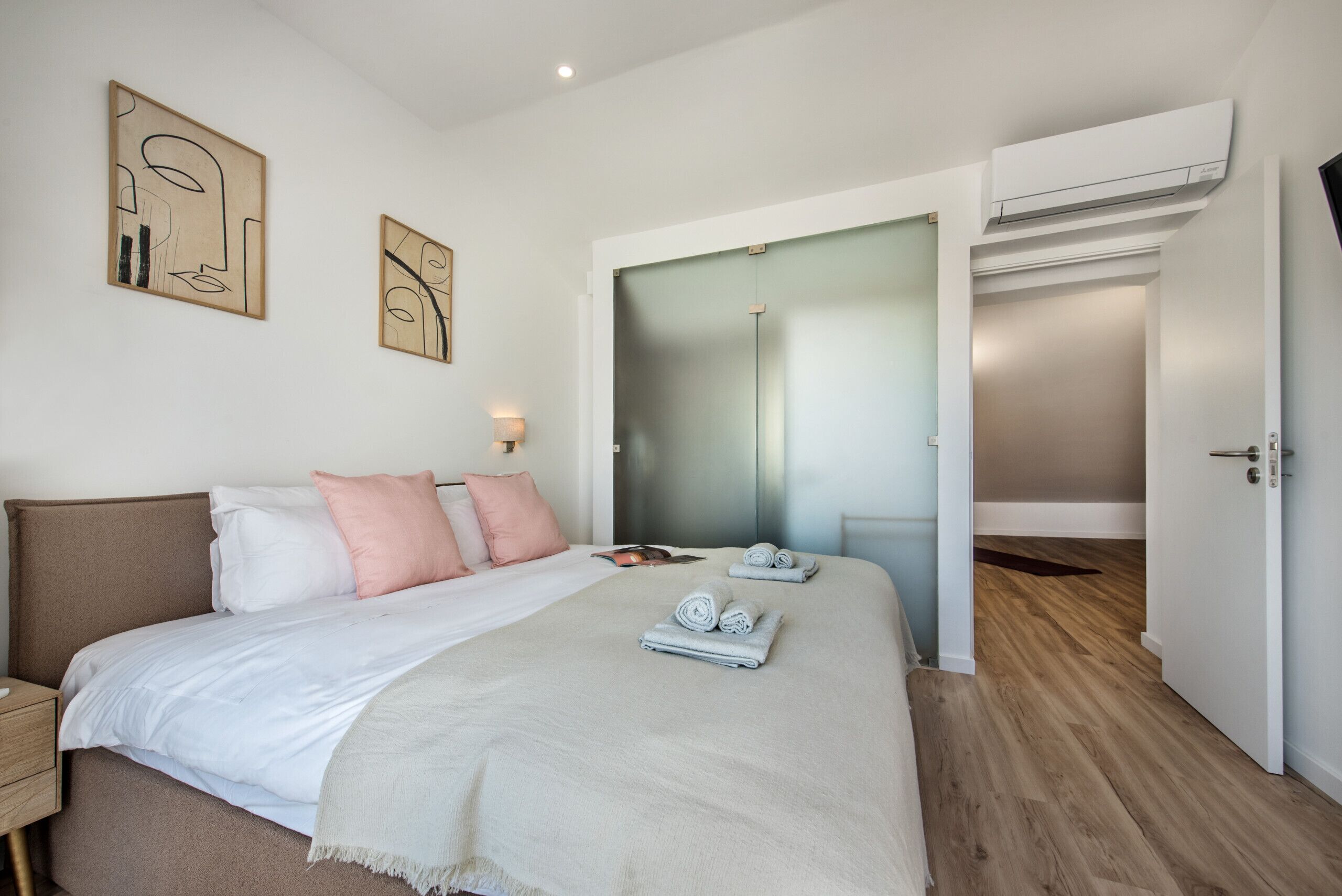 A modern bedroom with a bed, bedside tables, artwork, and a walk-in closet.