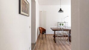 Ein Essbereich mit einem Holztisch, transparenten Stühlen, einem braunen Sessel, einer Pendelleuchte und einem gerahmten Bild an der Wand.