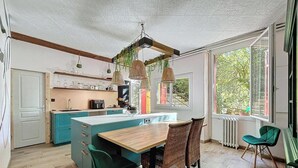 A kitchen with a central island, wooden ceiling beams, hanging wicker lamps, and a view of greenery outside. - Magnificent villa with breathtaking views, swimming pool, Jacuzzi 35min from the beaches. (Bédarieux)