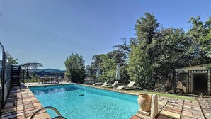 A rectangular swimming pool with a clear blue water surface, surrounded by a wooden deck. There are lounge chairs and umbrellas along the poolside. - Magnificent villa with breathtaking views, swimming pool, Jacuzzi 35min from the beaches. (Bédarieux)