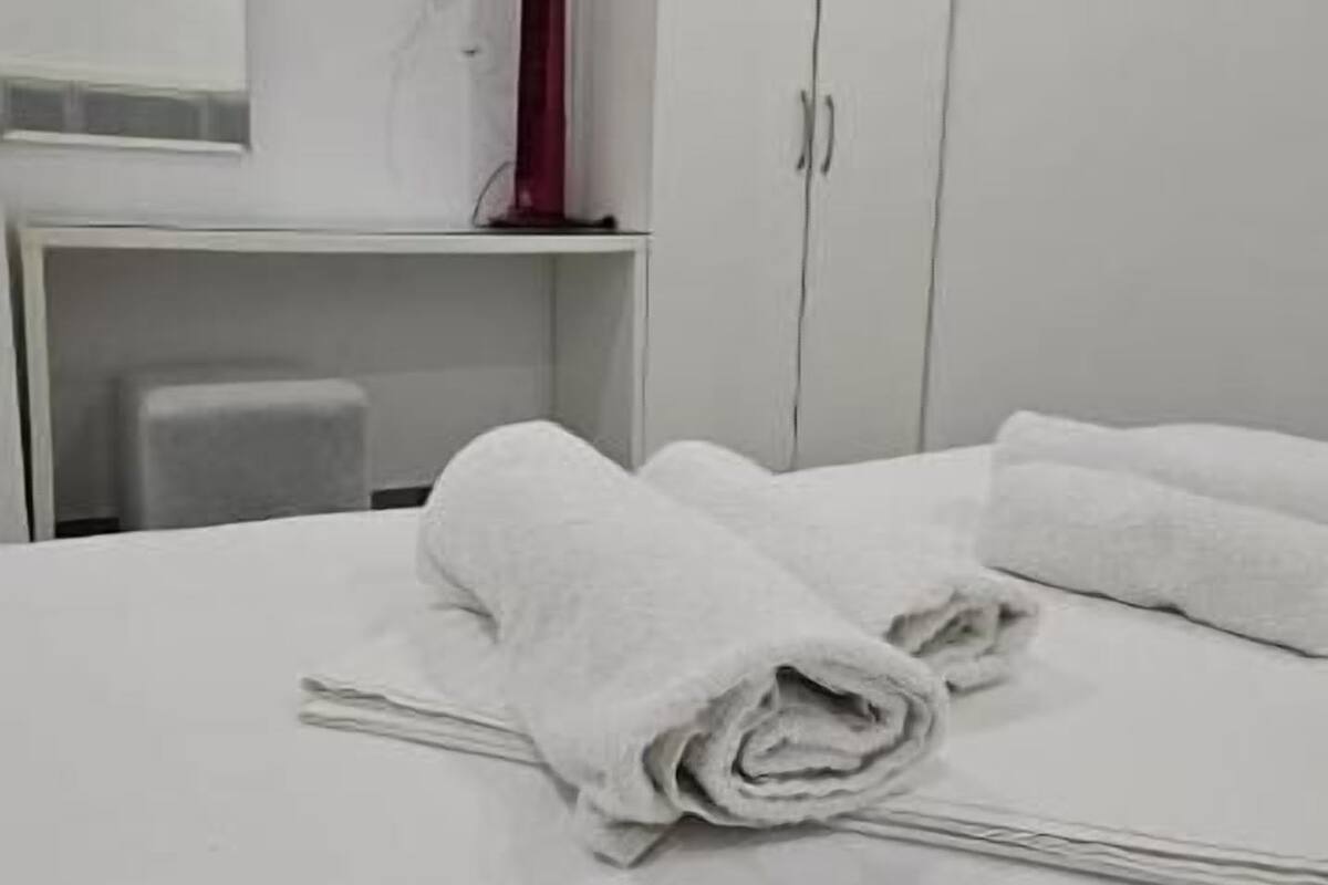 Una habitació d'hotel amb un llit, un armari blanc, una taula de treball amb una cadira i un objecte vermell sobre la taula.