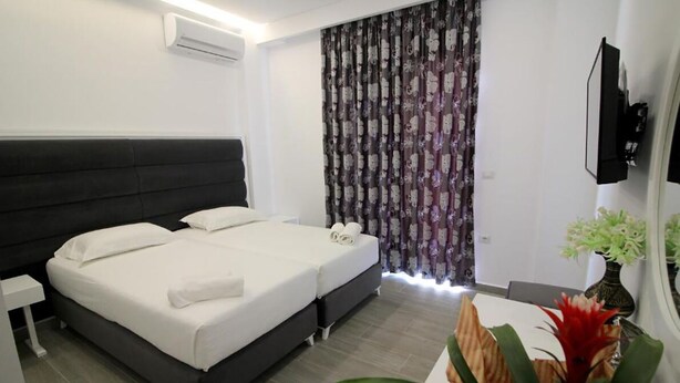 A hotel room with a bed, a nightstand, a TV, and a curtain. - Hotel Edina by Hp (Sarande)