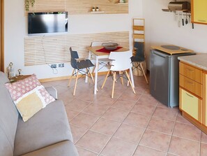 Ein gemütlicher Wohnbereich mit Sofa, Esstisch, Stühlen, einem über dem Tisch montierten Fernseher, einem Kühlschrank und einer Küchenarbeitsplatte.