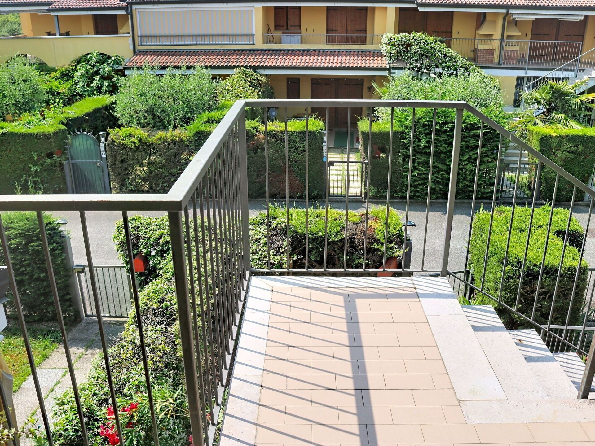 Un edifici residencial amb diversos pisos, un balcó, baranes metàl·liques i vegetació ben cuidada.