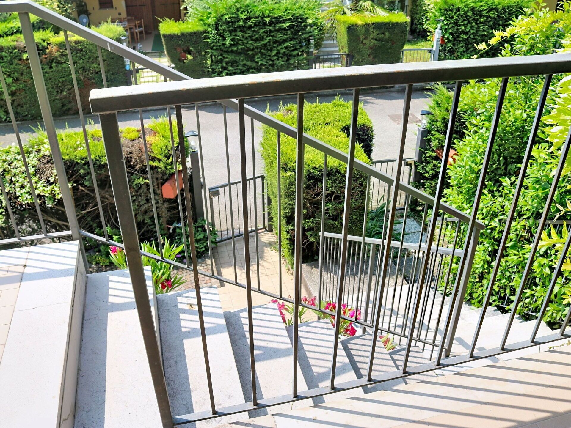 Une rambarde métallique offrant une vue sur un jardin et un bâtiment en arrière-plan.