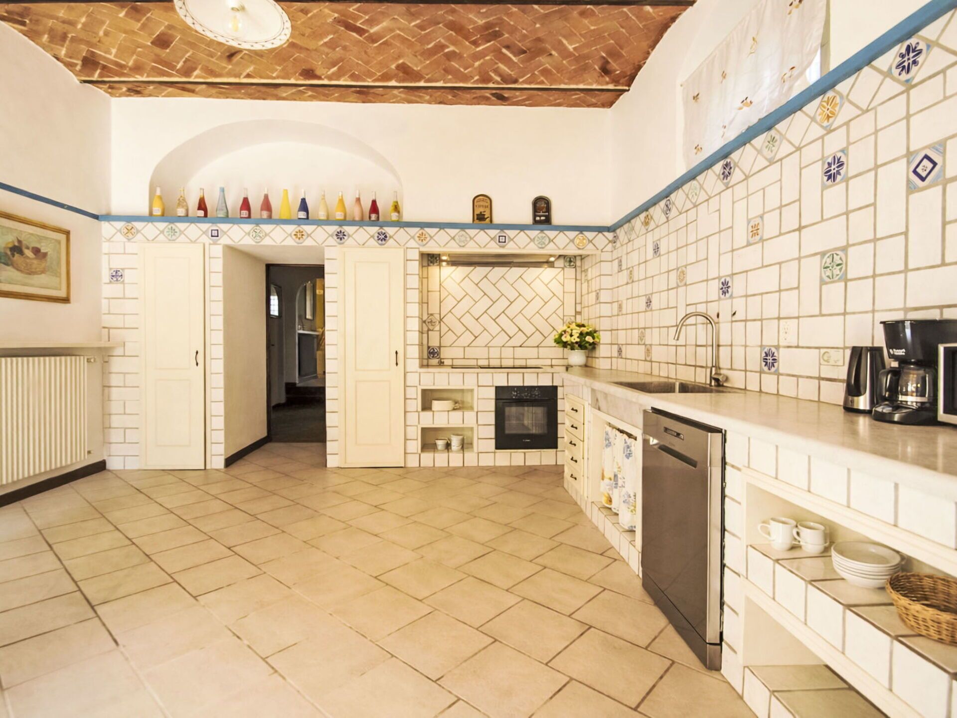 A kitchen with a herringbone-patterned backsplash, a dishwasher, a coffee maker, and a tiled floor.