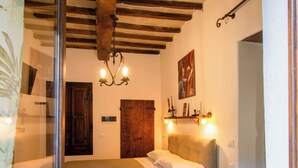 A bedroom with a bed, a wooden door, a chandelier, a painting, and a shelf with candles.