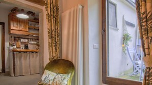 A room with a green armchair, a radiator, a window with a view of the outside, and a kitchen area in the background.