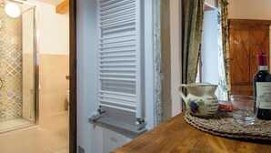 A room with a wooden table, a radiator, a patterned shower curtain, and a bottle of Castiglione wine.