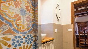 Uma casa de banho com azulejos estampados, balcão de madeira, uma toalha e uma porta que dá para uma zona de refeições.