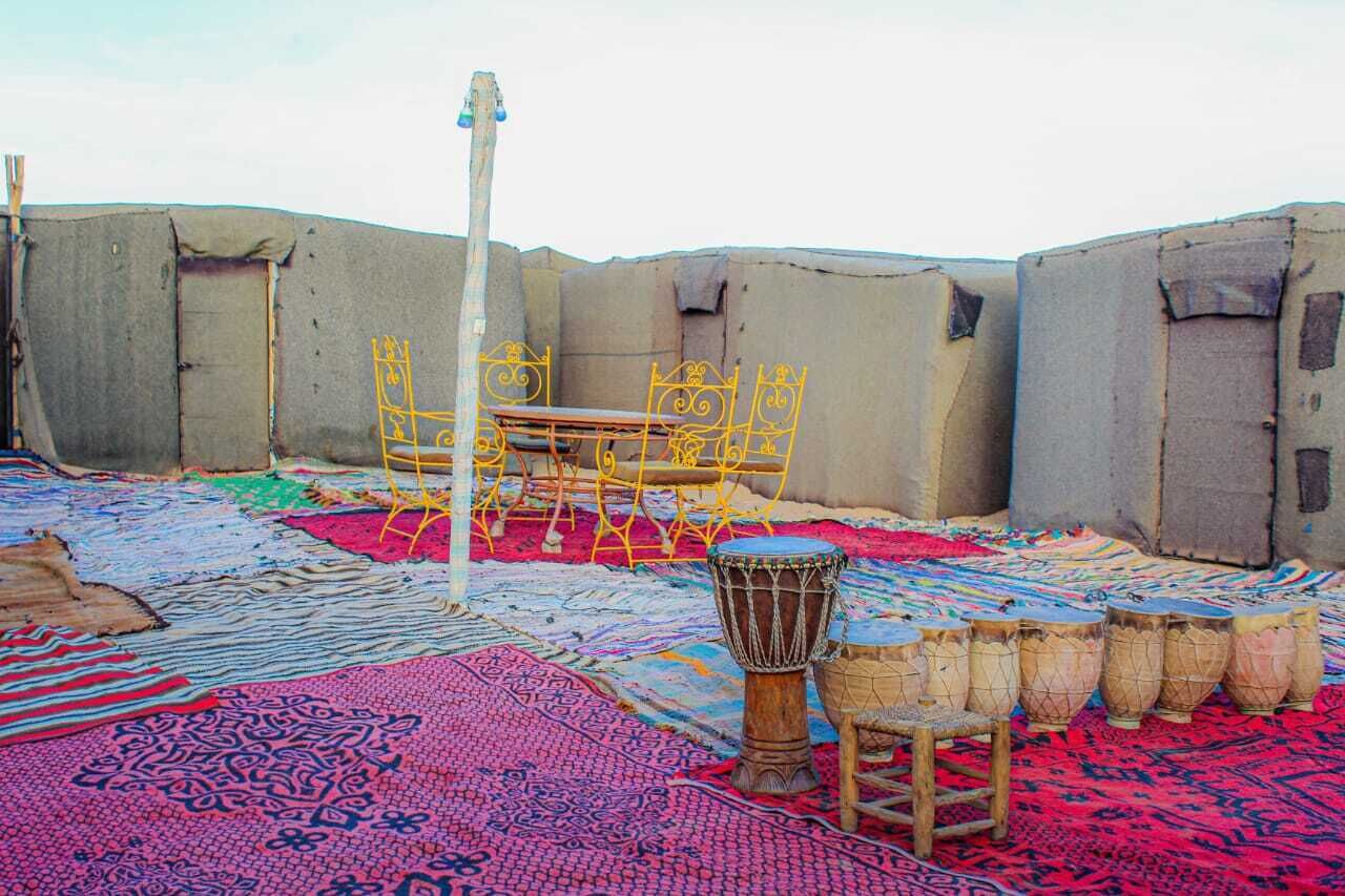 A courtyard with a table and chairs, a drum set, and colorful rugs.