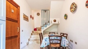Un comedor con una mesa preparada para cuatro, una escalera con barandas azules y platos decorativos en la pared.