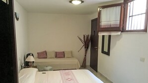 Un dormitorio con cama, mesita de noche, lámpara, sofá, ventana con cortina y puerta.