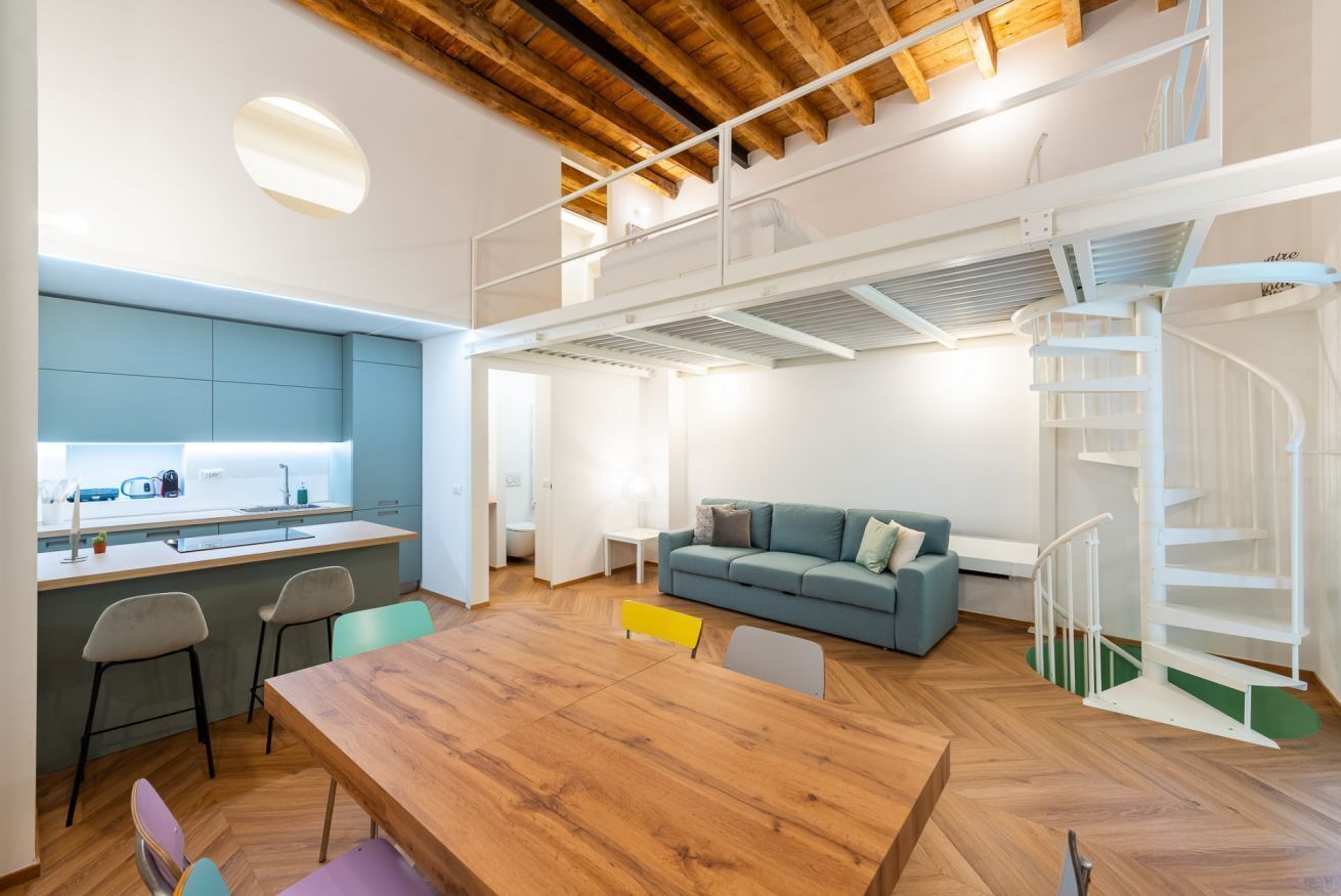 Un interior moderno con cocina, comedor y un dormitorio en entrepiso con escalera.
