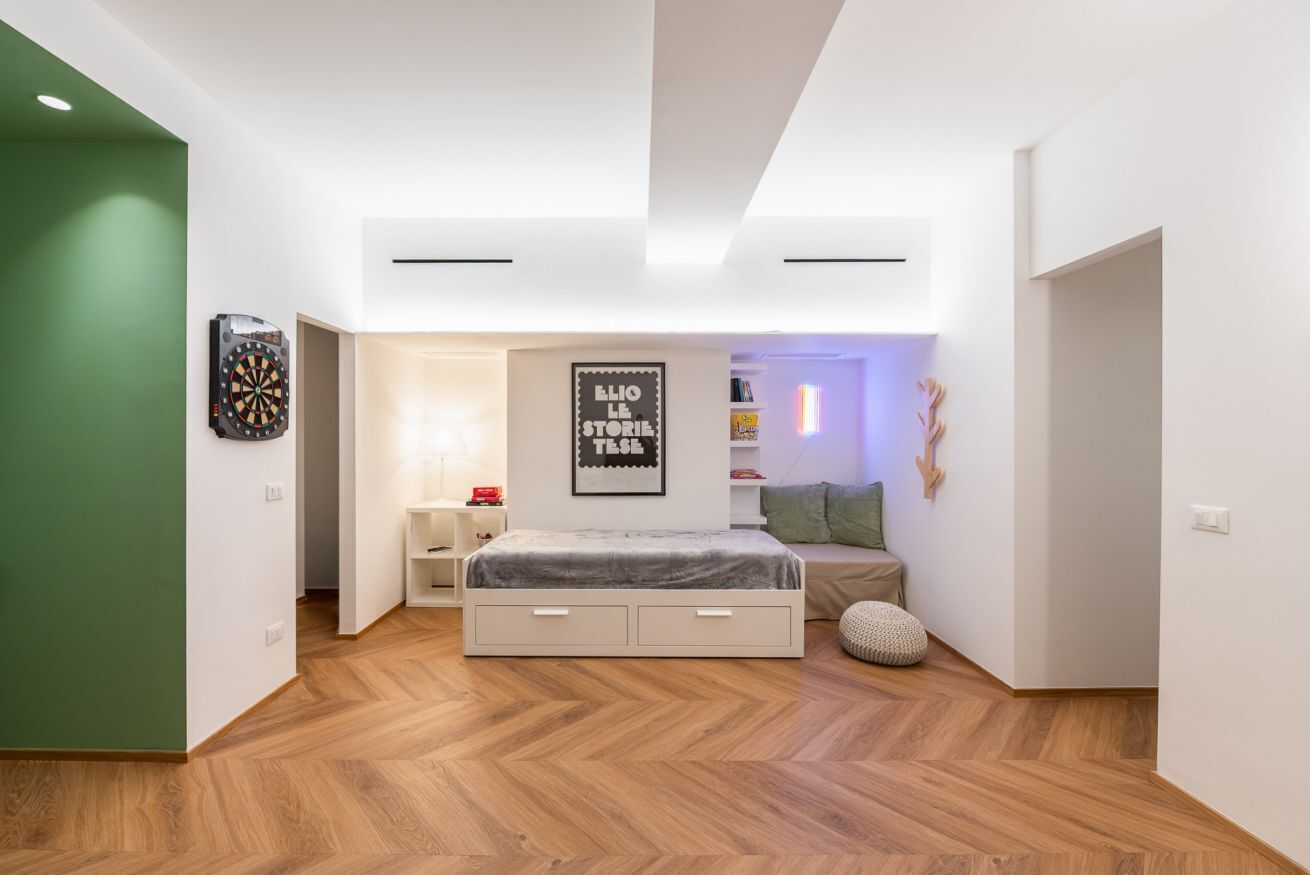 A modern bedroom with a bed, a dartboard, a wall-mounted poster, and a green wall.