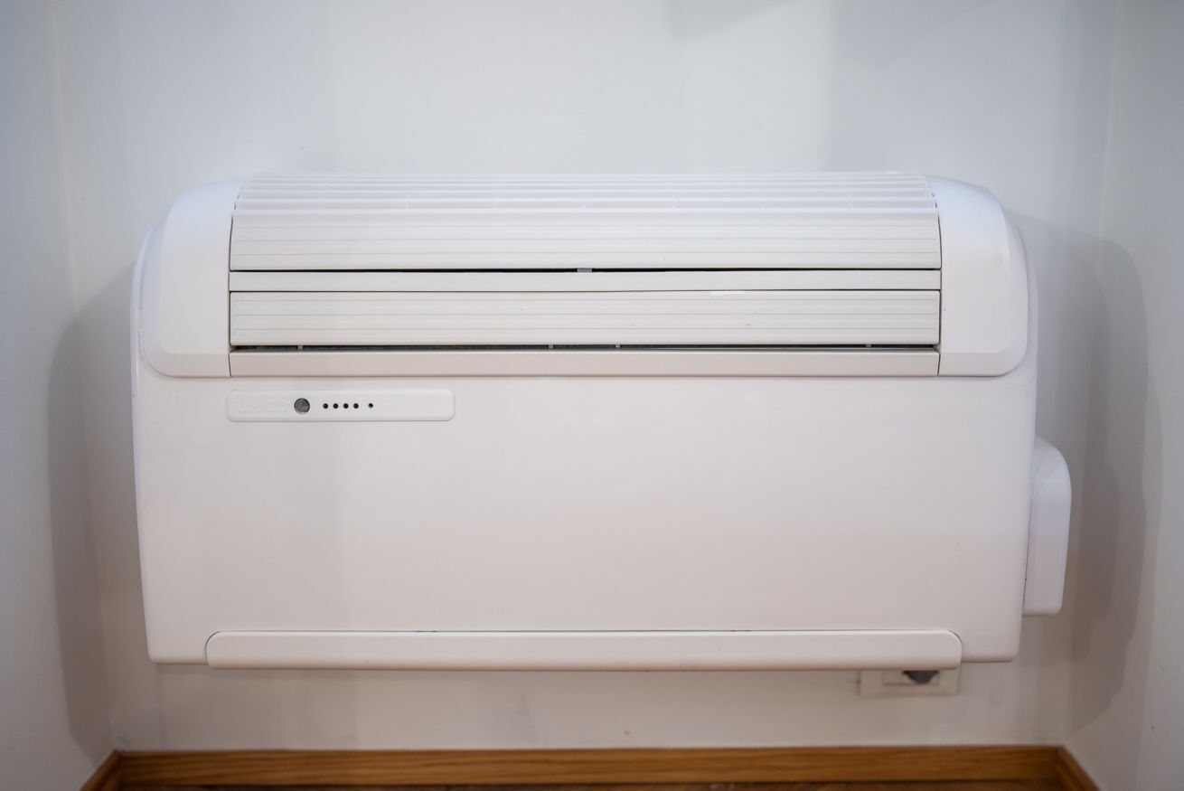 Un appareil de climatisation blanc, fixé au mur, doté d’un panneau de commande et d’une prise électrique située en dessous.