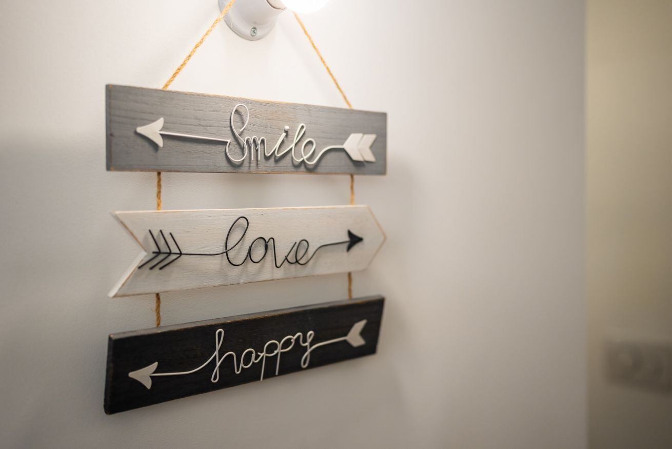 A wall-mounted sign with words 'Smile,' 'Love,' and 'Happy' each on a separate wooden arrow pointing to the right.