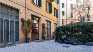 Un patio con una bicicleta, plantas en macetas y un edificio con contraventanas verdes.