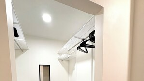 Un petit dressing étroit avec des étagères blanches, un miroir et un plancher en bois.