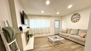 Un salon avec un canapé, une table basse, une cheminée, un téléviseur et une horloge au mur.