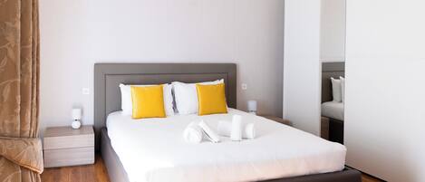 Moderni hotellihuone, jossa on suuri sänky, kaksi yöpöytää, yölamppu, vaatekaappi ja peili.