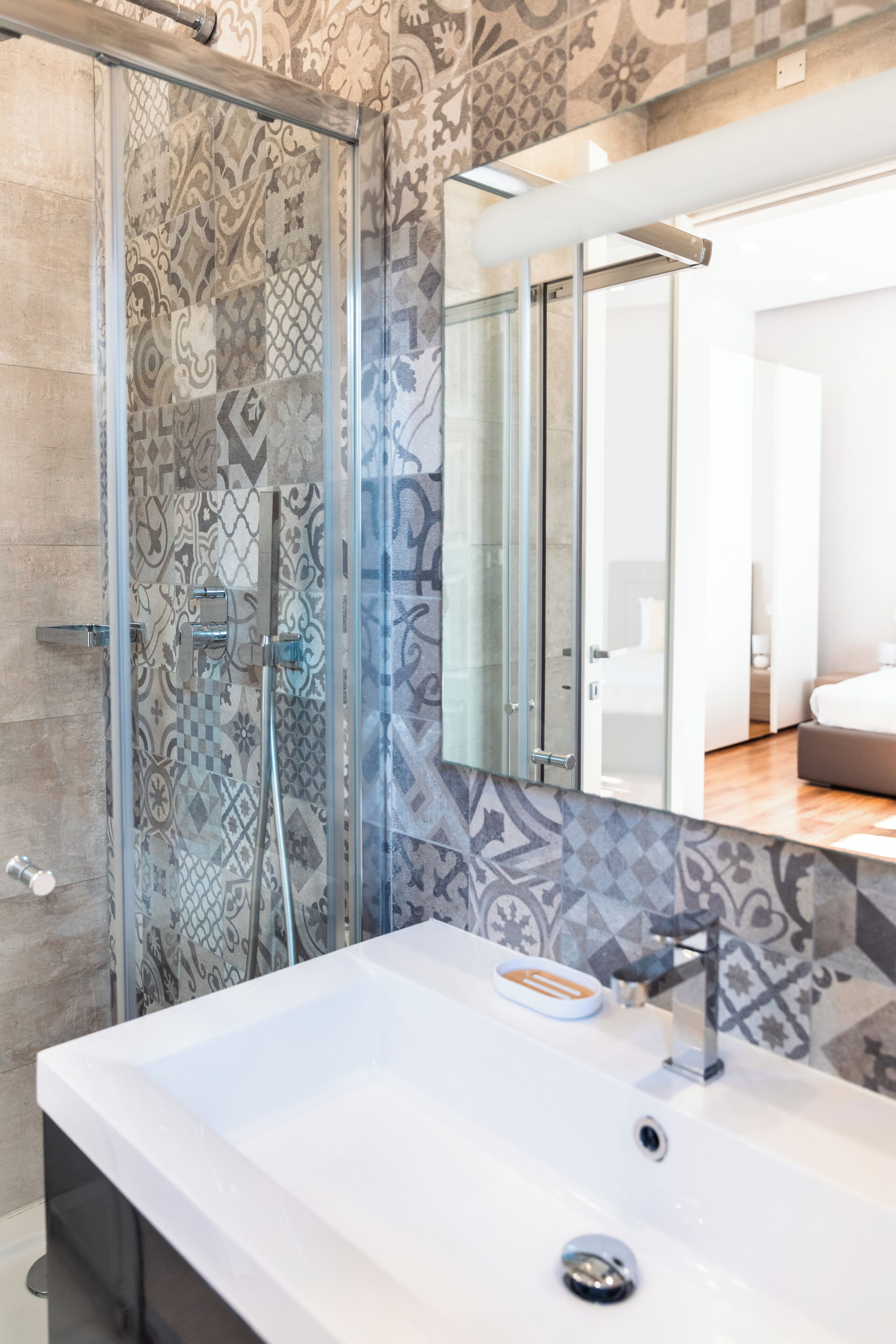 A modern bathroom with a glass shower enclosure, a white sink, and a patterned tile backsplash.