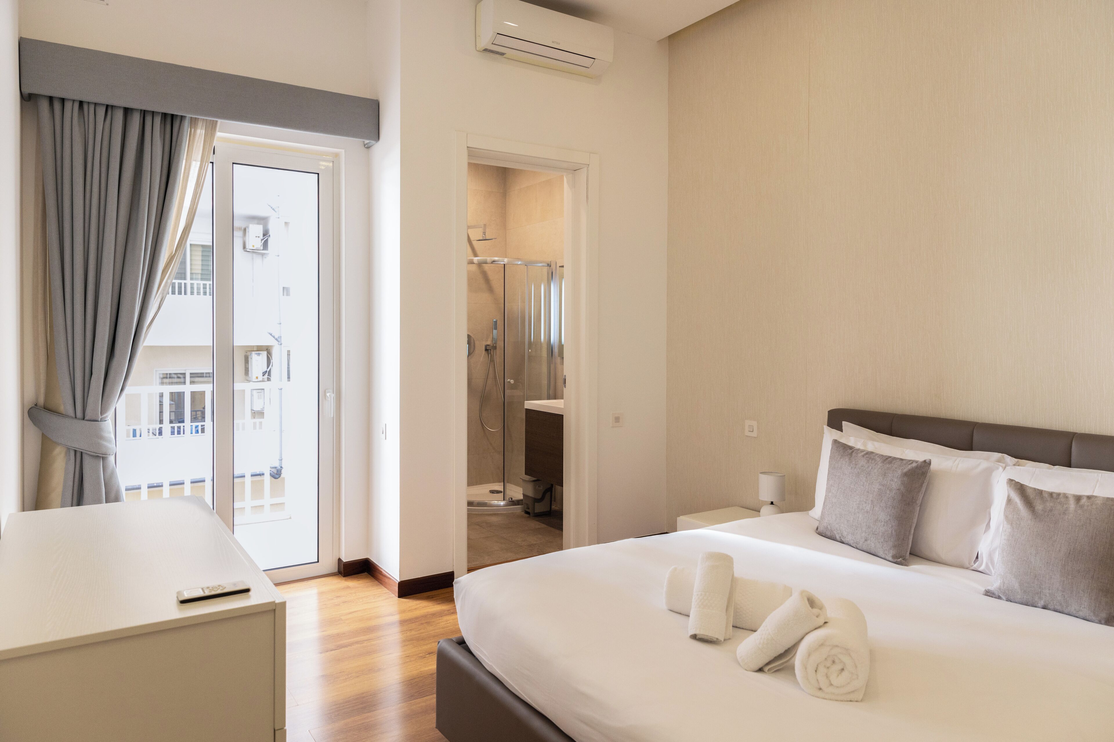 A hotel room with a bed, a desk, a bathroom with a shower, and a view of the outside.