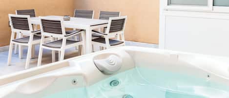 Un bain à remous avec une table et des chaises, installé dans un espace extérieur ensoleillé.
