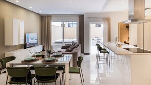 A modern kitchen with a central island, a dining area with a glass table, and a living space with a sofa and large windows. - Duplex Sliema (Sliema)