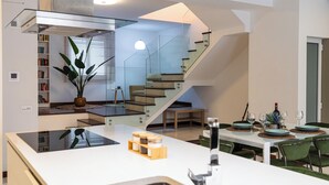 A modern kitchen with a central island, a dining area with green chairs, and a staircase leading to another level. - Duplex Sliema (Sliema)