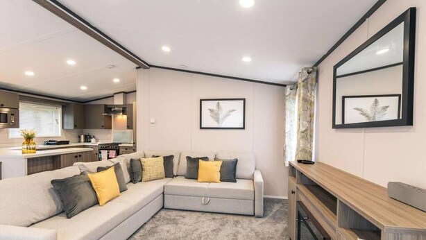 A modern living area with a sectional sofa, a wooden console table, and a kitchen in the background. - Fox Lodge with Hot tub (york)