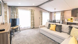 A modern living room with a sofa, TV, and dining area. - Fox Lodge with Hot tub (york)