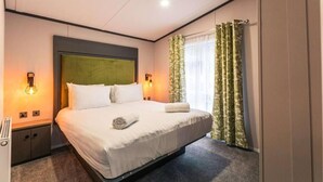 A hotel room with a bed, two bedside lamps, a window with curtains, and a headboard. - Fox Lodge with Hot tub (york)