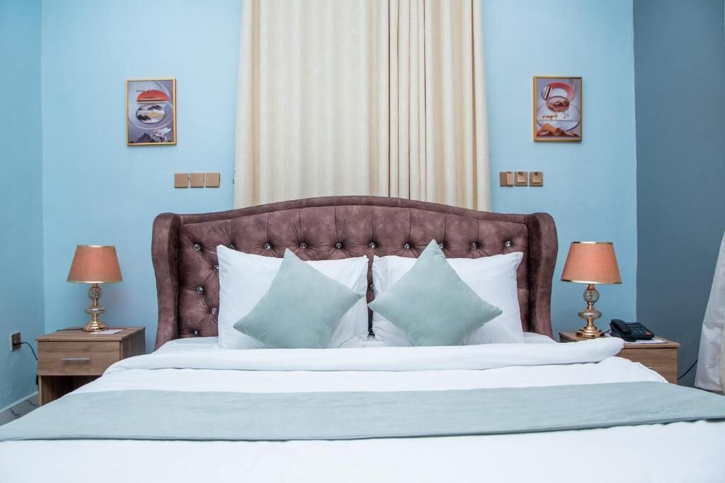 A bedroom with a tufted headboard, two bedside lamps, a bed with white bedding, and two wall-mounted light switches.