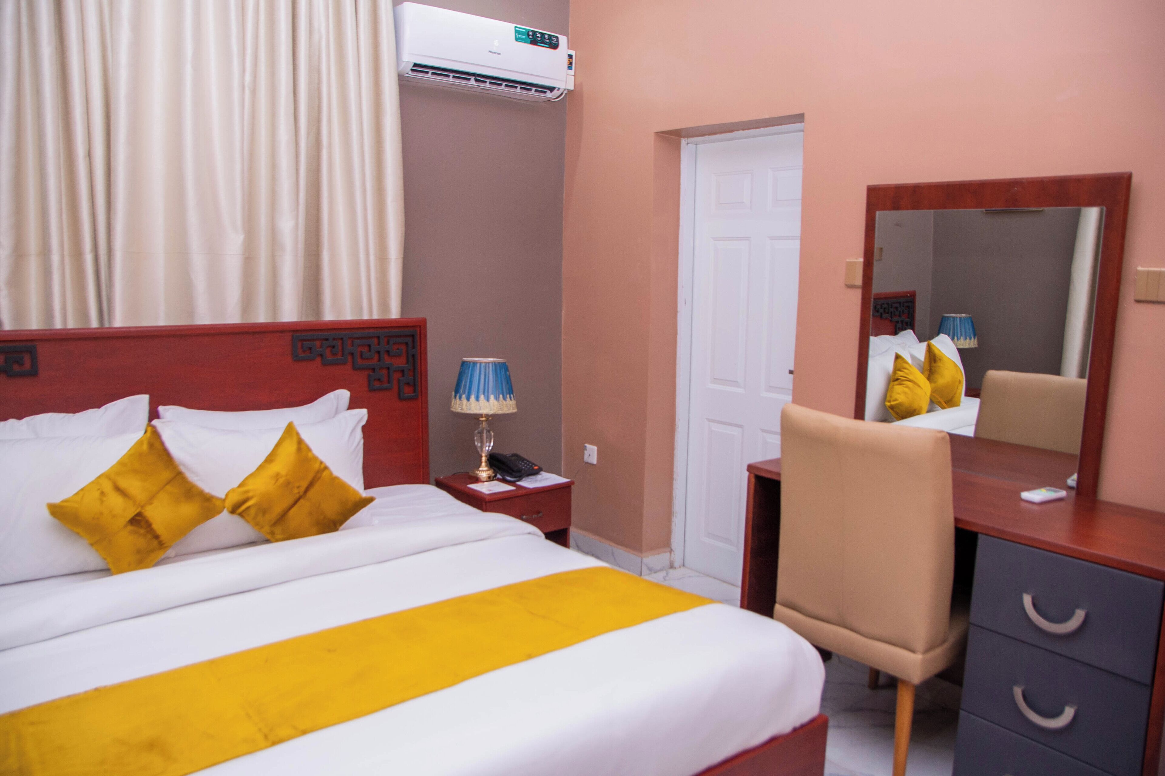 A hotel room with a bed, a desk, a chair, a mirror, and a door.