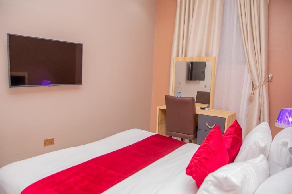 Ein Hotelzimmer mit Bett, Schreibtisch, Stuhl, Spiegel und Fernseher.