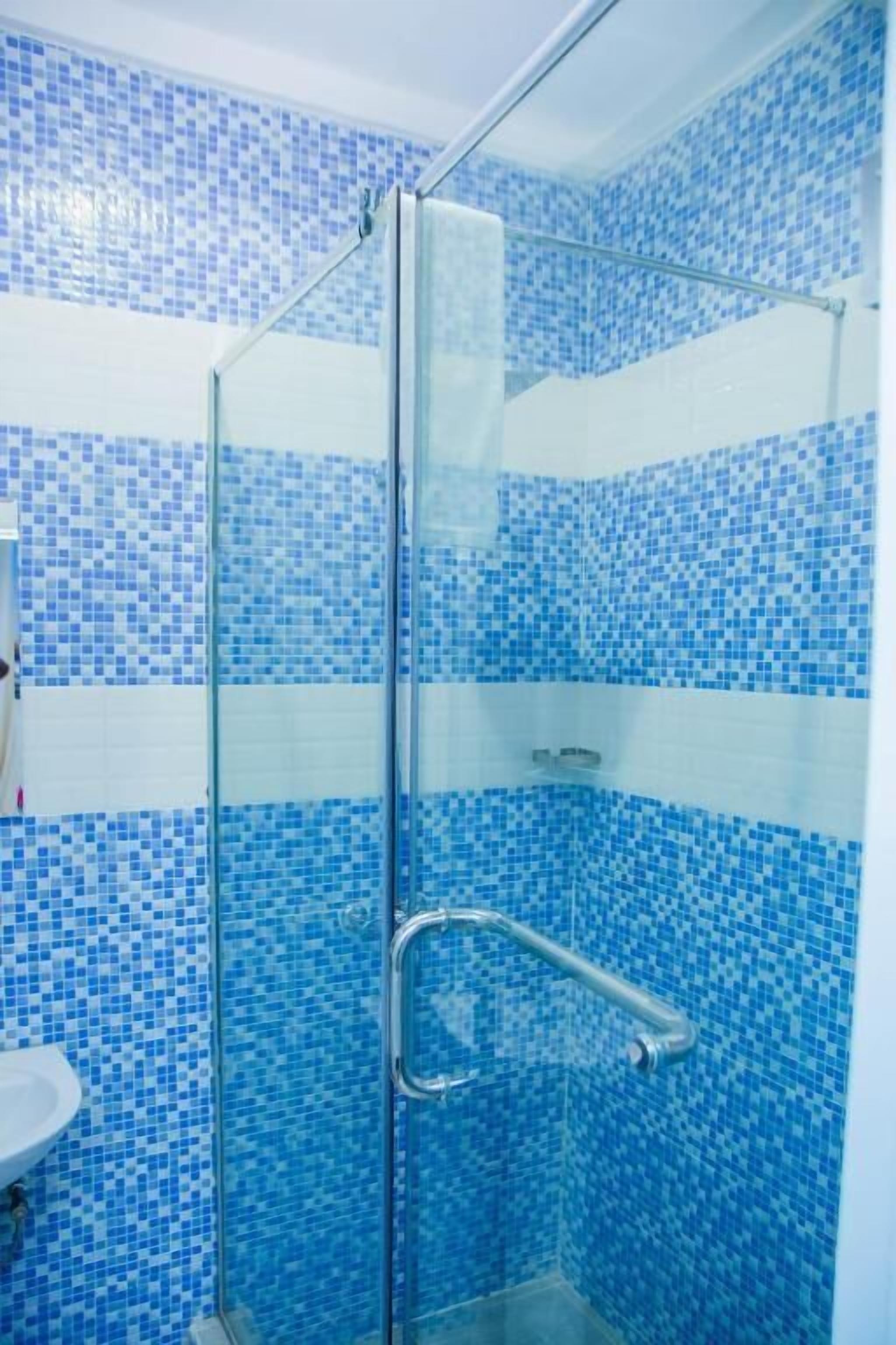 Ein Badezimmer mit blauen Mosaikfliesen, einer Duschkabine aus Glas und einem weißen Waschbecken.