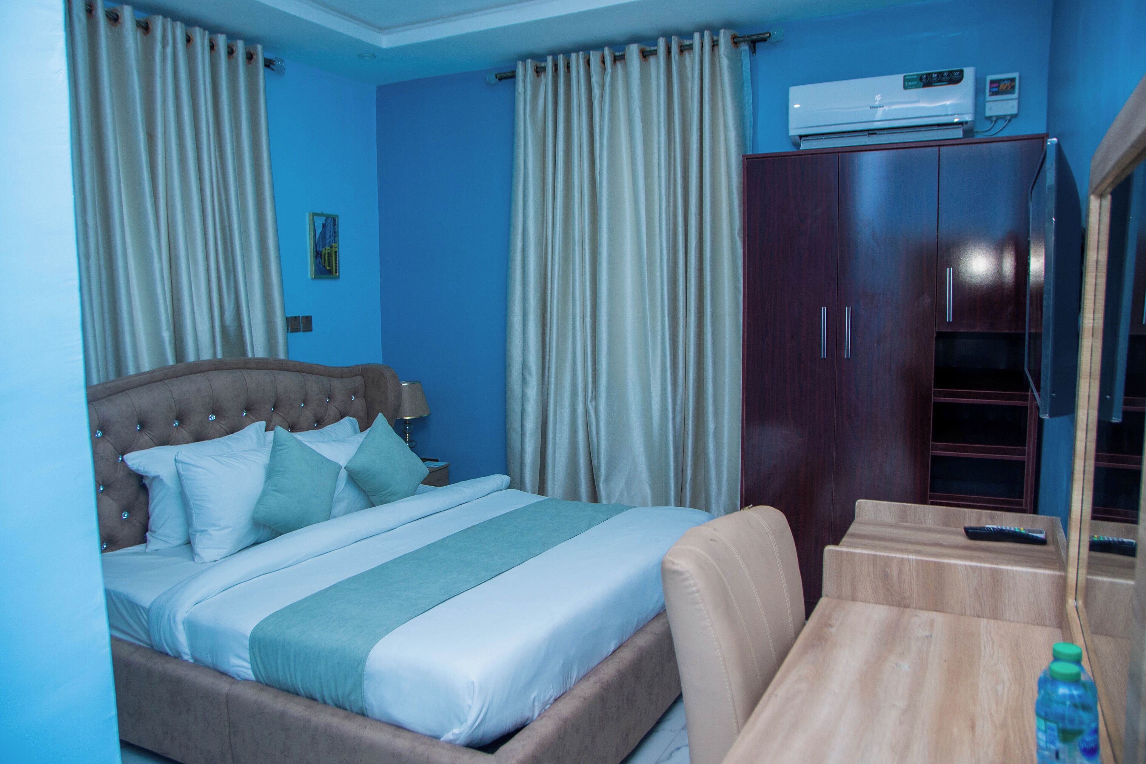 Una habitación de hotel con cama, cortinas, un armario, una mesa y un control remoto.