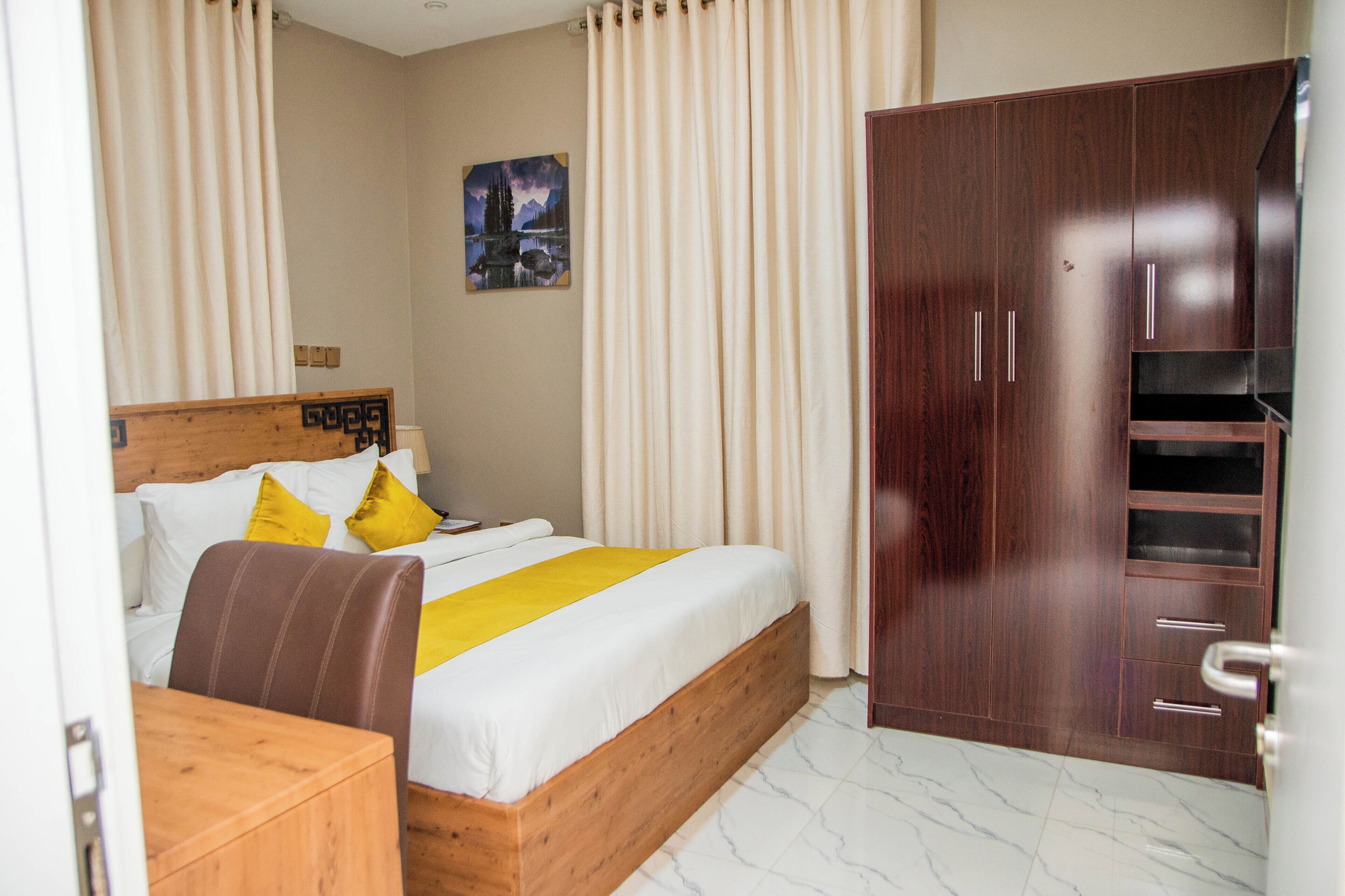 A bedroom with a bed, wooden headboard, curtains, a wardrobe, and a painting on the wall.