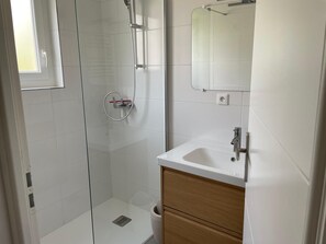 Ein modernes Badezimmer mit Duschkabine aus Glas, einem weißen Waschbecken und einem Holzwaschtisch.