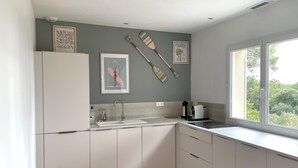 Une cuisine avec des meubles blancs, un évier, une cuisinière et une fenêtre donnant sur un paysage verdoyant.