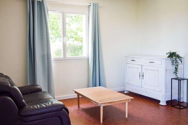 Une pièce avec un canapé en cuir, une table en bois, une armoire blanche et une fenêtre avec des rideaux.