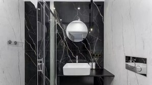 Un baño moderno con pared de mármol, lavamanos blanco y espejo.