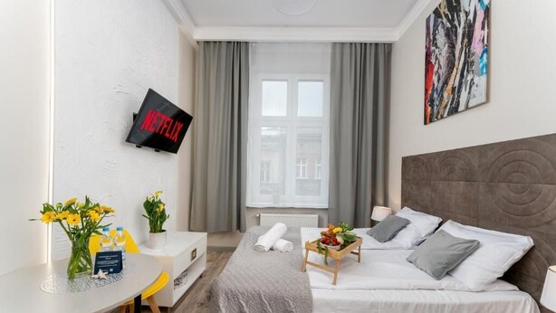 Habitación de hotel con cama, escritorio, televisión montada en la pared y ventana con cortinas.