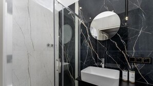 Un baño moderno con cabina de ducha de vidrio, lavamanos blanco y salpicadero de mármol.