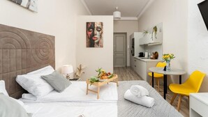 Una habitación de hotel moderna con una cama, una mesita con frutas, una silla, un escritorio y una zona de cocina.