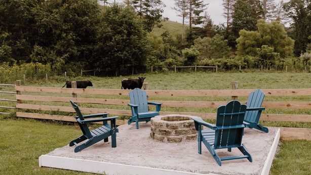 Area esterna recintata con poltrone Adirondack e un braciere in pietra.